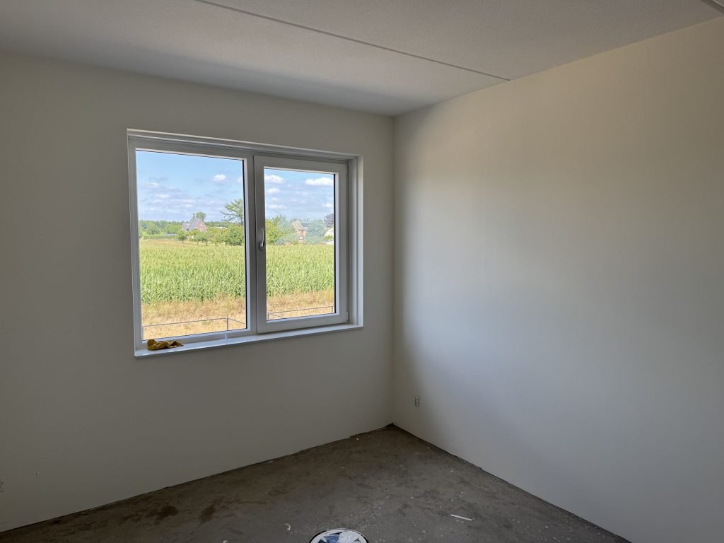 Lege kamer met gladde, lichte wanden en een raam, klaar om behangen te worden