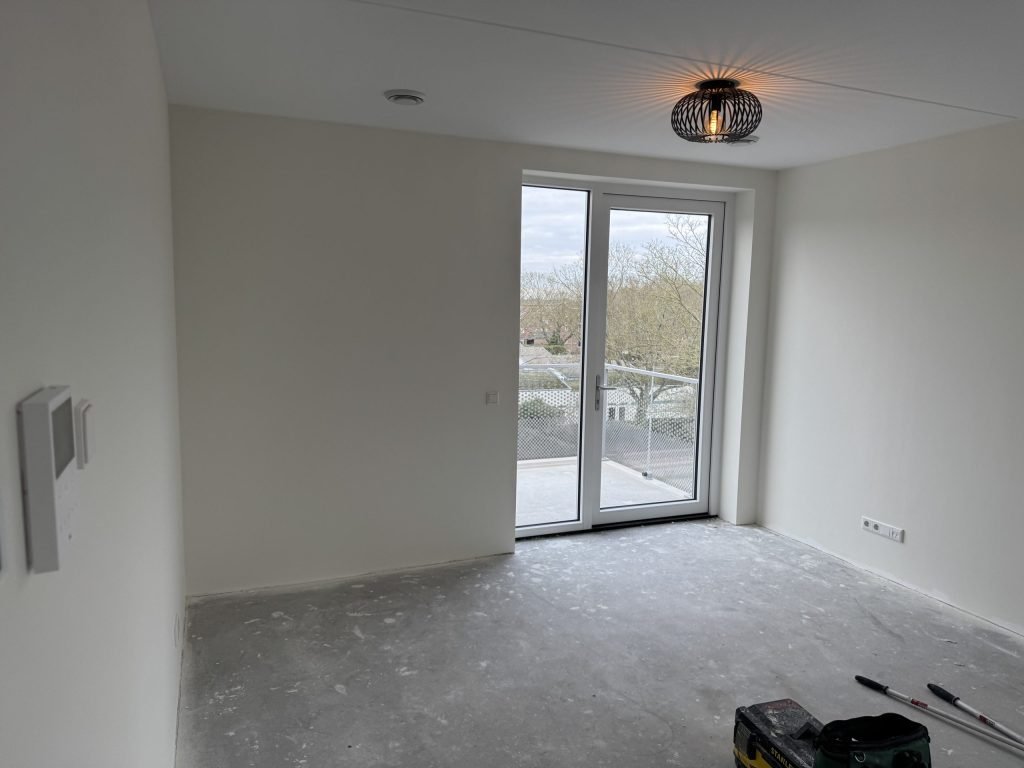 Lege kamer met openslaande deuren en kale wanden, kort na de oplevering